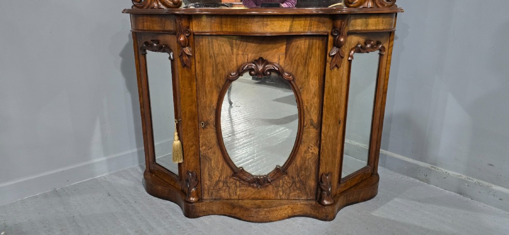 An antique burr walnut side cabinet featuring an arched top mirror with a carved cresting and glass mirrored door panels. View X