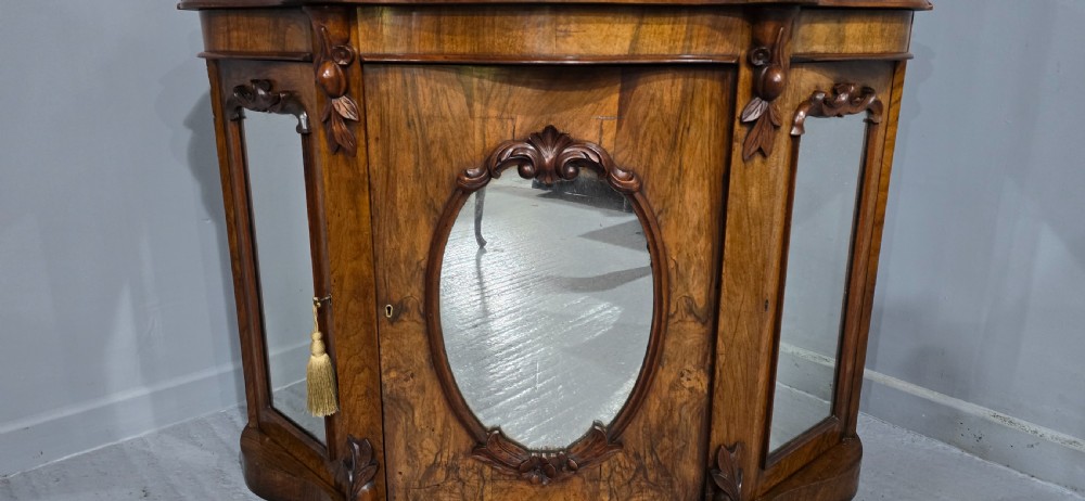 An antique burr walnut side cabinet featuring an arched top mirror with a carved cresting and glass mirrored door panels. View XI