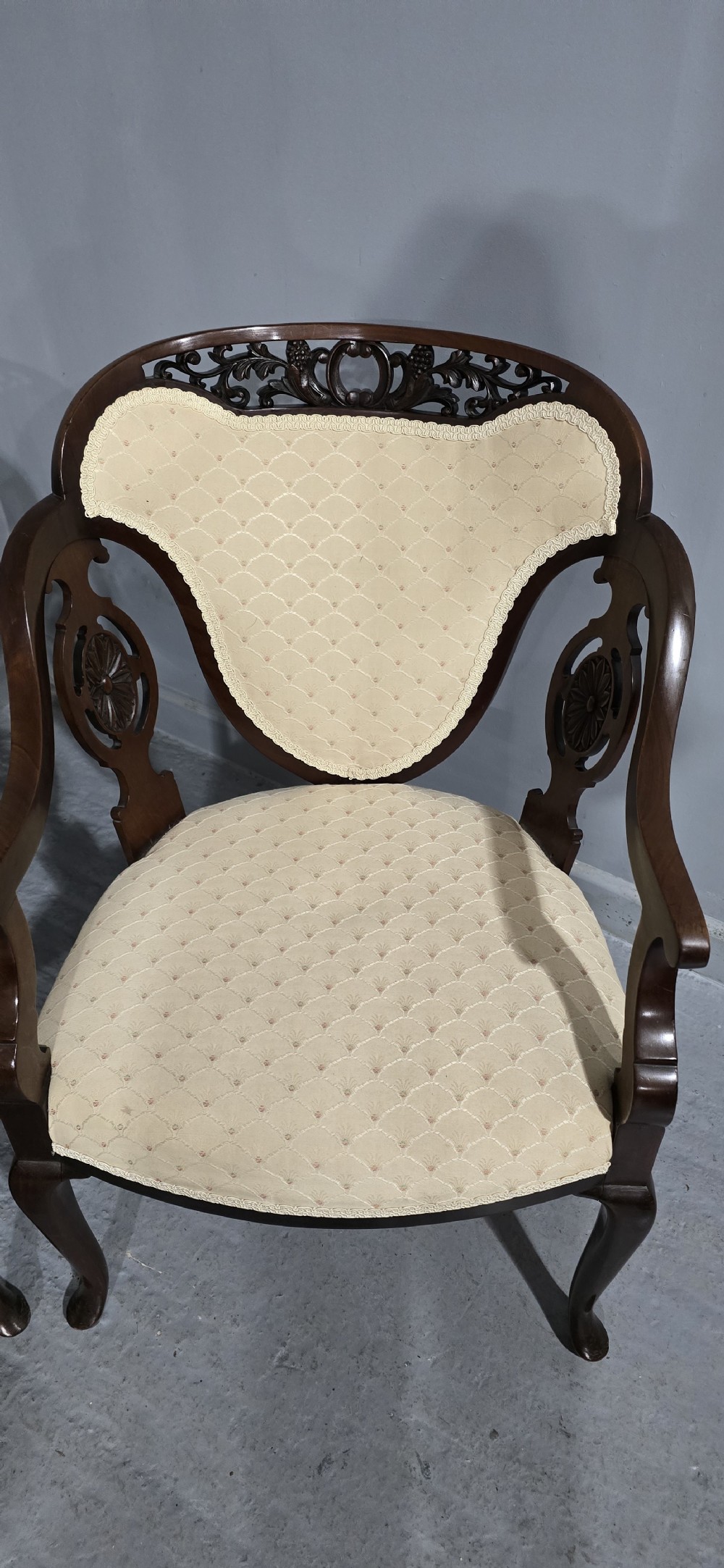 A pair of antique Victorian mahogany elbow chairs featuring carved crest rails, pierced arm supports, cabriole legs, and cream upholstered seats. View II