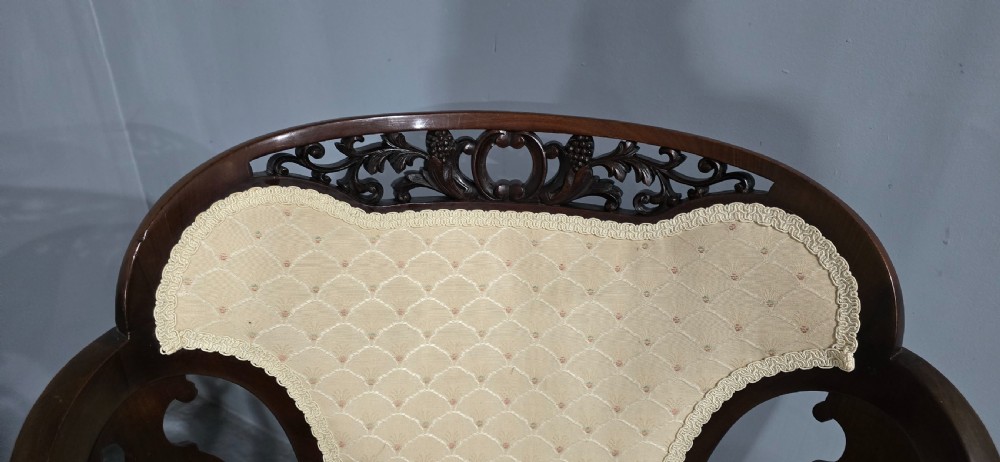 A pair of antique Victorian mahogany elbow chairs featuring carved crest rails, pierced arm supports, cabriole legs, and cream upholstered seats. View V