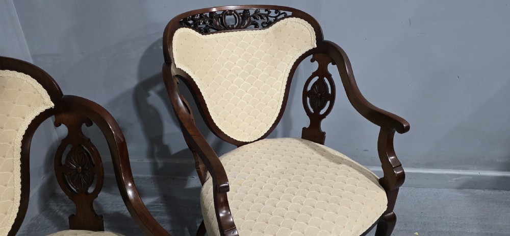 A pair of antique Victorian mahogany elbow chairs featuring carved crest rails, pierced arm supports, cabriole legs, and cream upholstered seats. View VII
