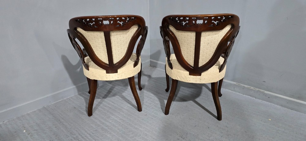 A pair of antique Victorian mahogany elbow chairs featuring carved crest rails, pierced arm supports, cabriole legs, and cream upholstered seats. View IX