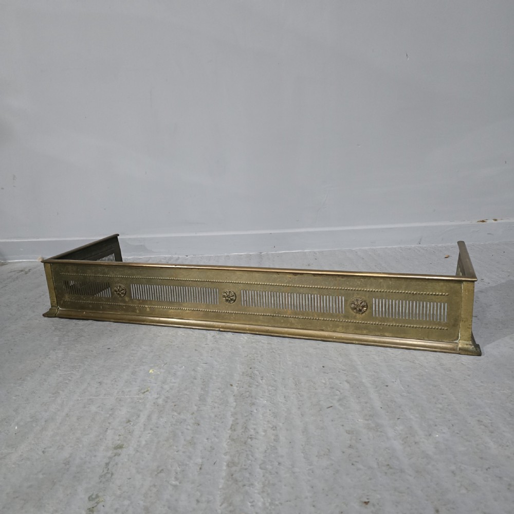 A Regency period brass fireplace fender featuring pierced vertical slots and cast rosette details along the front rail.