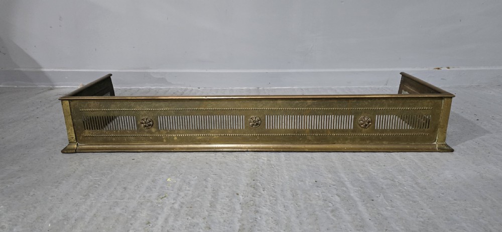 A Regency period brass fireplace fender featuring pierced vertical slots and cast rosette details along the front rail. View II