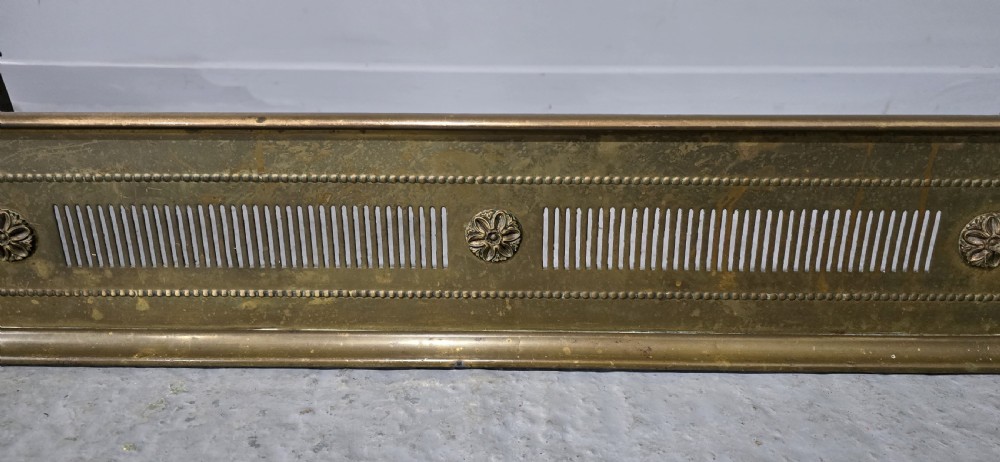 A Regency period brass fireplace fender featuring pierced vertical slots and cast rosette details along the front rail. View III