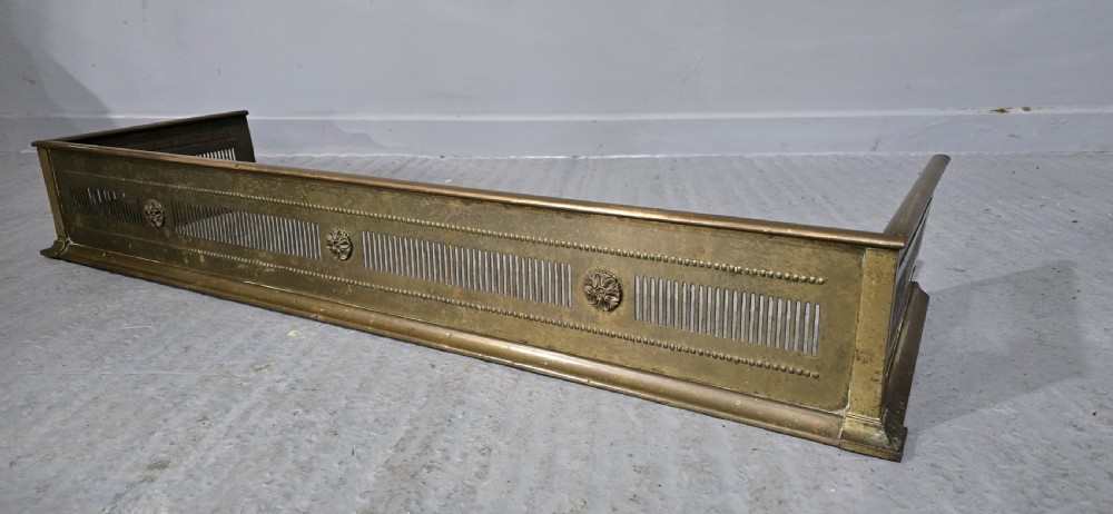 A Regency period brass fireplace fender featuring pierced vertical slots and cast rosette details along the front rail. View IV