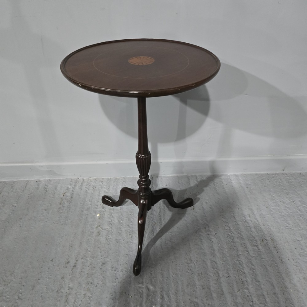 A round mahogany wine table featuring an inlaid central starburst motif, a turned column pedestal, and three splayed legs.