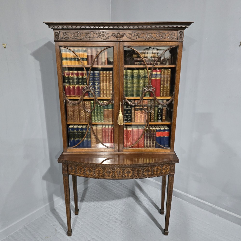 An Adam style mahogany bookcase on stand featuring carved urn frieze ornamentation, astragal glazed doors, and slender tapered legs. View II