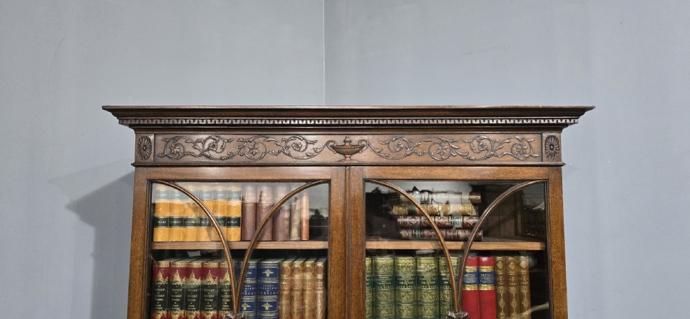 An Adam style mahogany bookcase on stand featuring carved urn frieze ornamentation, astragal glazed doors, and slender tapered legs. View III