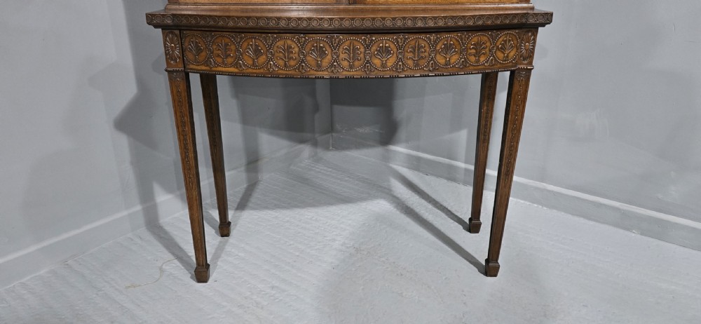 An Adam style mahogany bookcase on stand featuring carved urn frieze ornamentation, astragal glazed doors, and slender tapered legs. View VII