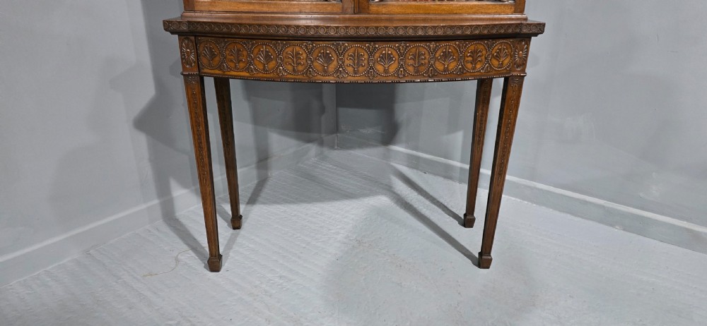 An Adam style mahogany bookcase on stand featuring carved urn frieze ornamentation, astragal glazed doors, and slender tapered legs. View VIII
