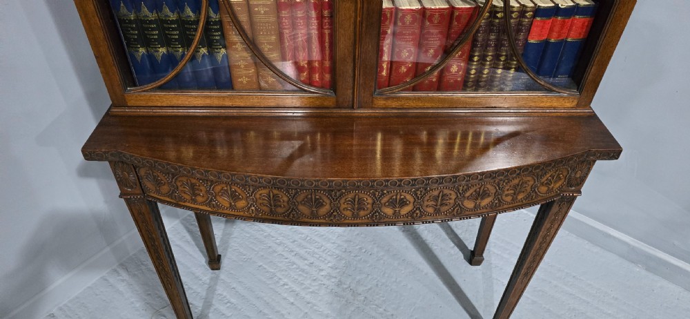An Adam style mahogany bookcase on stand featuring carved urn frieze ornamentation, astragal glazed doors, and slender tapered legs. View IX
