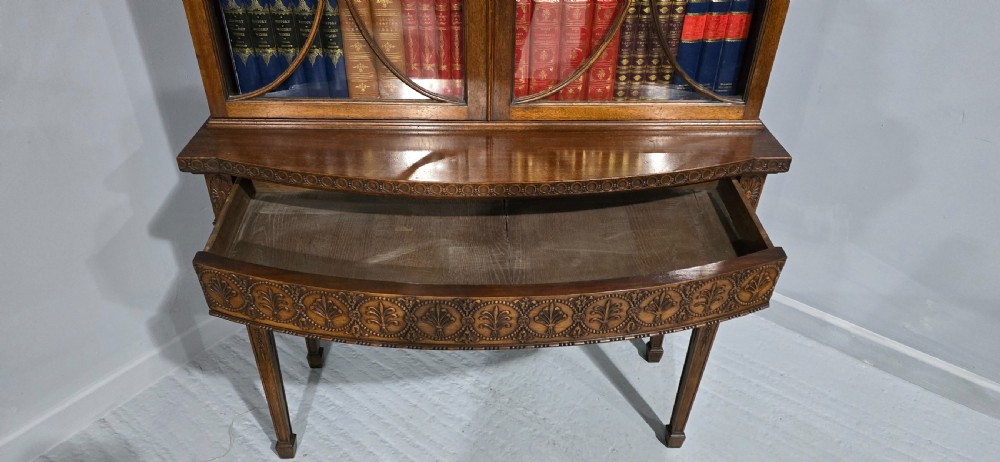 An Adam style mahogany bookcase on stand featuring carved urn frieze ornamentation, astragal glazed doors, and slender tapered legs. View X