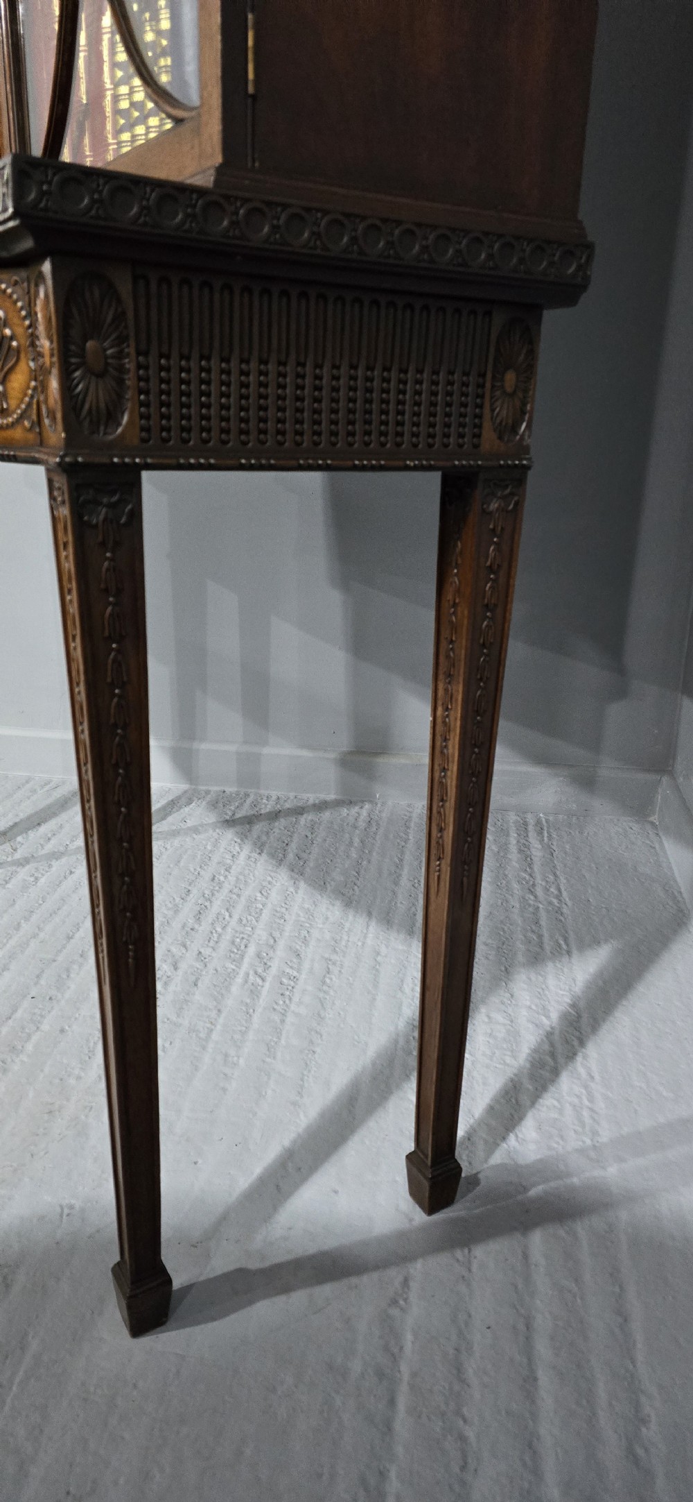An Adam style mahogany bookcase on stand featuring carved urn frieze ornamentation, astragal glazed doors, and slender tapered legs. View XIII