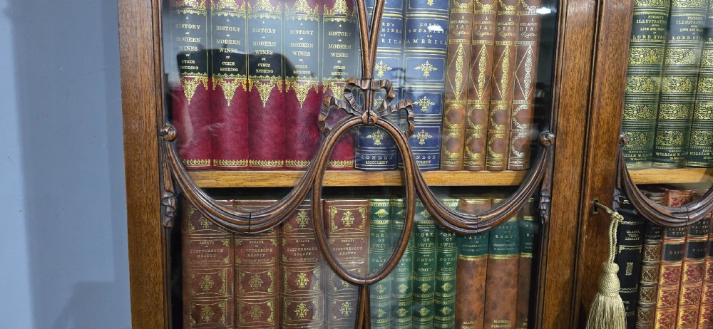 An Adam style mahogany bookcase on stand featuring carved urn frieze ornamentation, astragal glazed doors, and slender tapered legs. View XVII