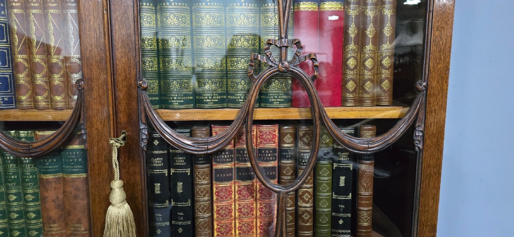 An Adam style mahogany bookcase on stand featuring carved urn frieze ornamentation, astragal glazed doors, and slender tapered legs. View XVIII