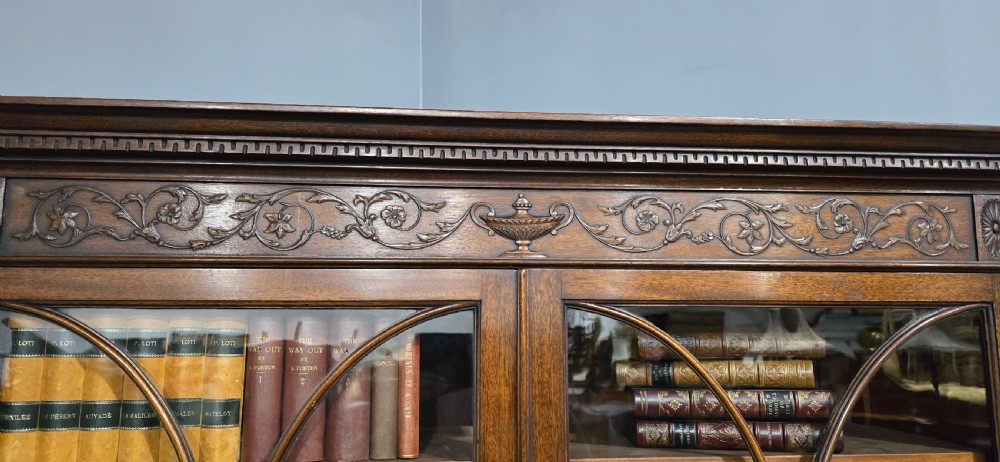 An Adam style mahogany bookcase on stand featuring carved urn frieze ornamentation, astragal glazed doors, and slender tapered legs. View XIX