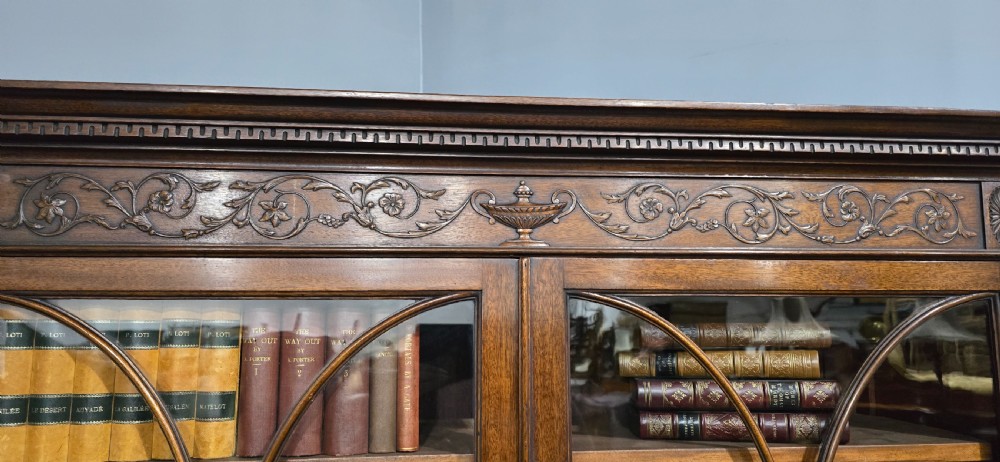 An Adam style mahogany bookcase on stand featuring carved urn frieze ornamentation, astragal glazed doors, and slender tapered legs. View XX