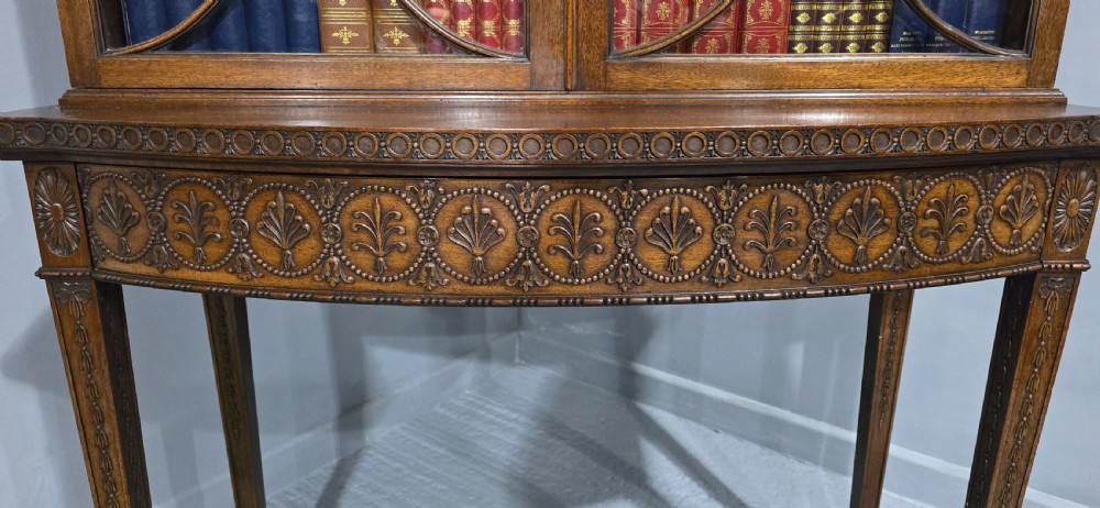An Adam style mahogany bookcase on stand featuring carved urn frieze ornamentation, astragal glazed doors, and slender tapered legs. View XXI