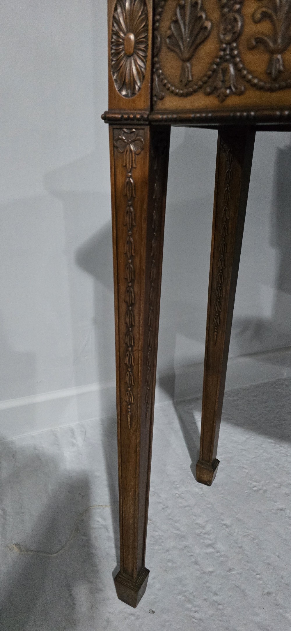 An Adam style mahogany bookcase on stand featuring carved urn frieze ornamentation, astragal glazed doors, and slender tapered legs. View XXII