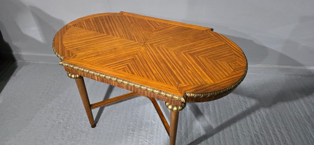An oval satinwood coffee table featuring a parquetry top, gilt egg-and-dart rim moulding, fluted tapered legs, and an X-frame stretcher. View II