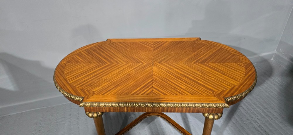An oval satinwood coffee table featuring a parquetry top, gilt egg-and-dart rim moulding, fluted tapered legs, and an X-frame stretcher. View IX