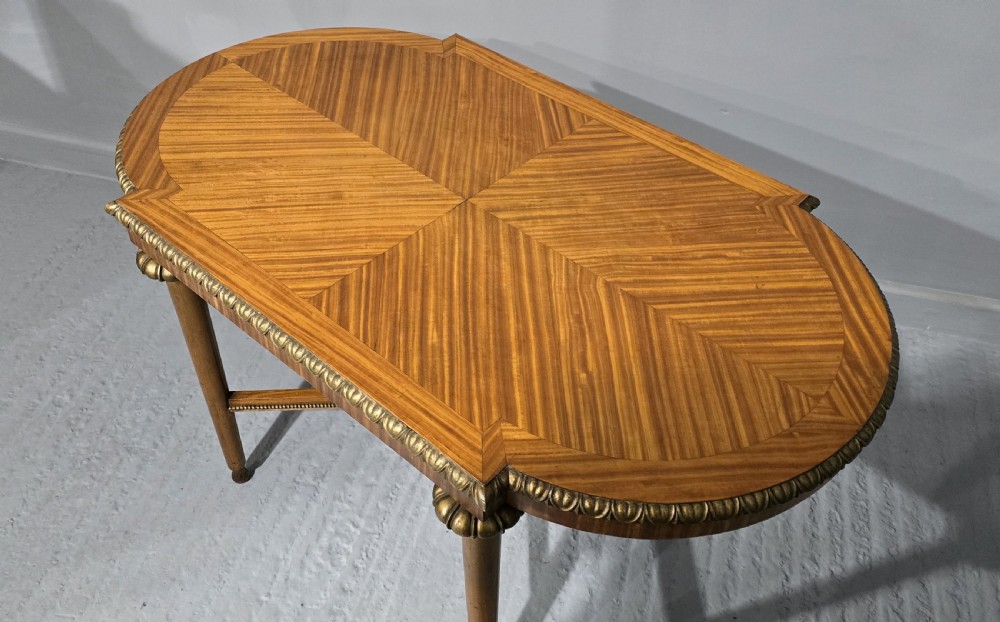 An oval satinwood coffee table featuring a parquetry top, gilt egg-and-dart rim moulding, fluted tapered legs, and an X-frame stretcher. View X