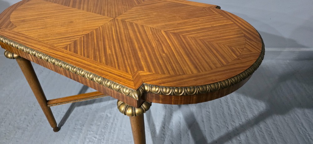 An oval satinwood coffee table featuring a parquetry top, gilt egg-and-dart rim moulding, fluted tapered legs, and an X-frame stretcher. View XI