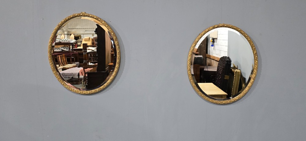 A pair of matching oval wall mirrors featuring molded gold gilt frames and bevelled glass plates. View II