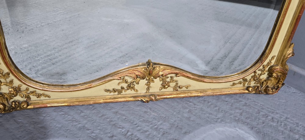 A large Victorian Rococo Revival giltwood and cream painted overmantel mirror featuring shell cresting, carved scrolls, and an arched glass plate. View V