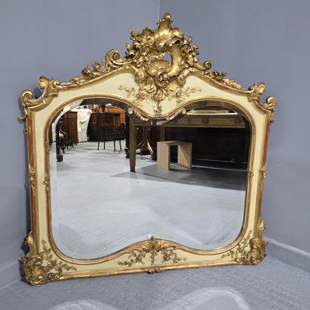 A large Victorian Rococo Revival giltwood and cream painted overmantel mirror featuring shell cresting, carved scrolls, and an arched glass plate. View II