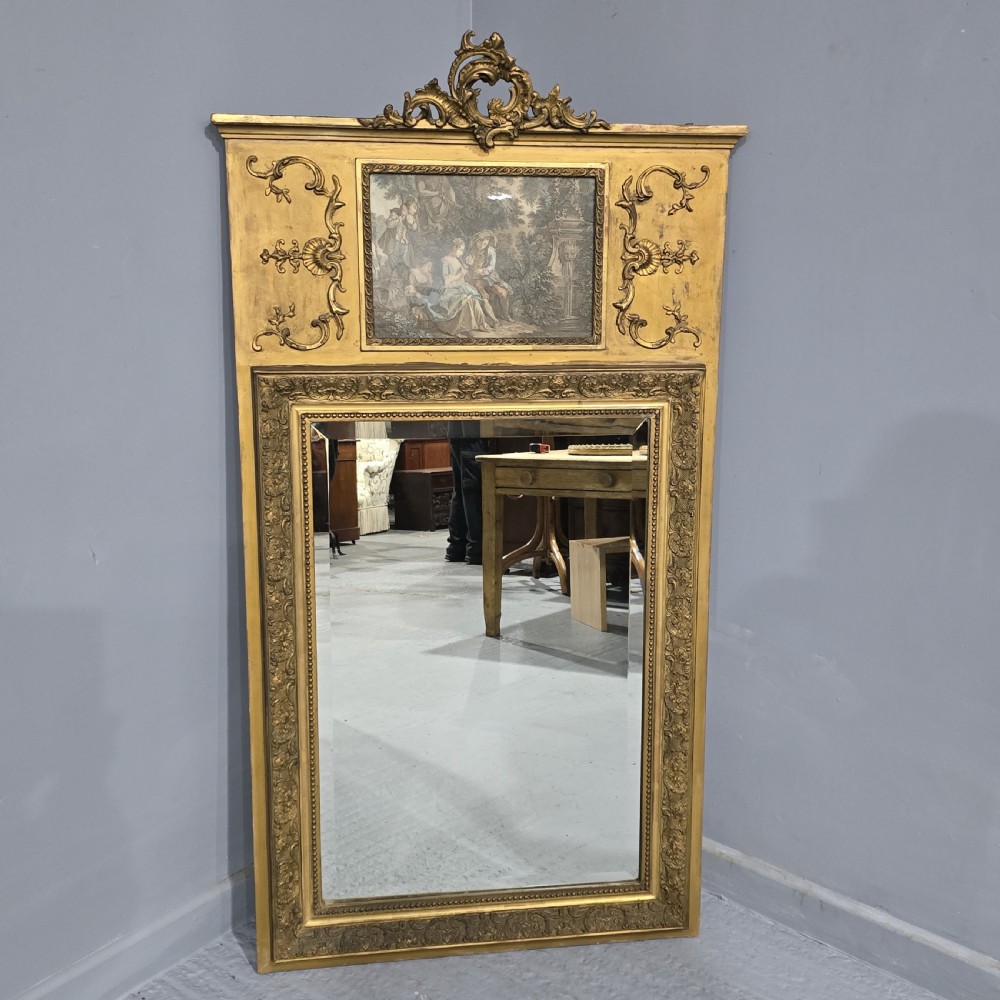 A tall gilded French trumeau mirror featuring a carved top pediment, an upper inset pastoral painting, and a rectangular mirror glass pane below.