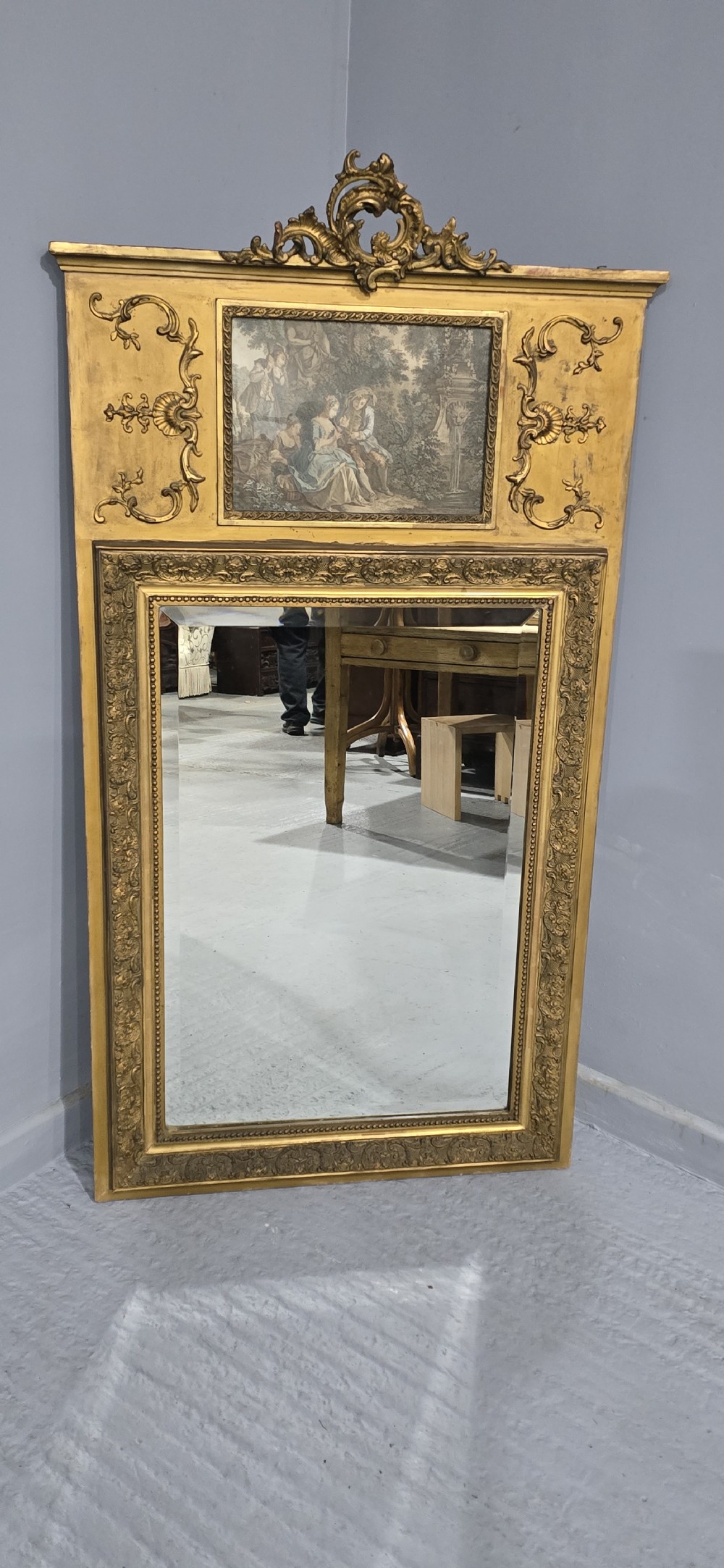 A tall gilded French trumeau mirror featuring a carved top pediment, an upper inset pastoral painting, and a rectangular mirror glass pane below. View II
