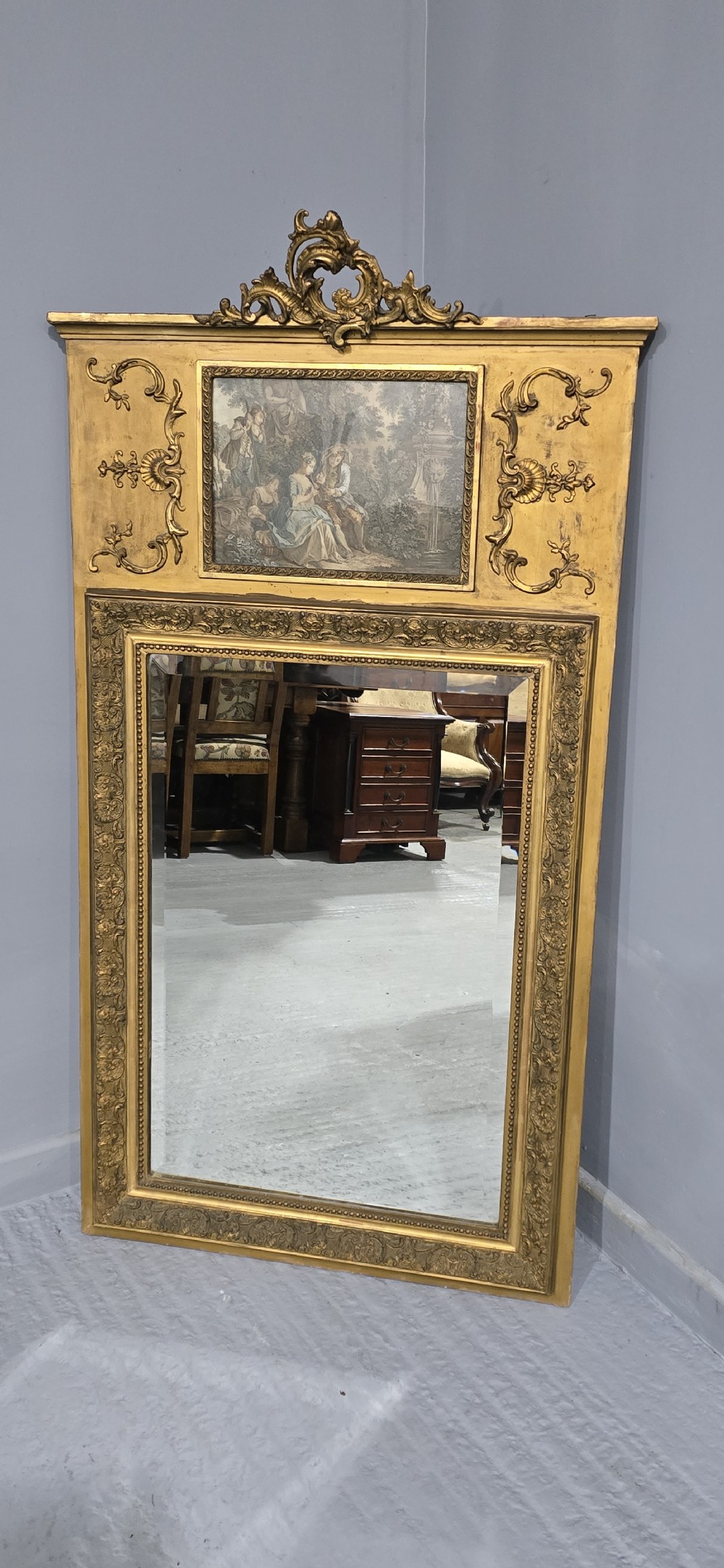 A tall gilded French trumeau mirror featuring a carved top pediment, an upper inset pastoral painting, and a rectangular mirror glass pane below. View III