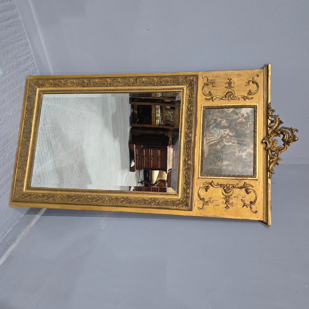 A tall gilded French trumeau mirror featuring a carved top pediment, an upper inset pastoral painting, and a rectangular mirror glass pane below. View VII
