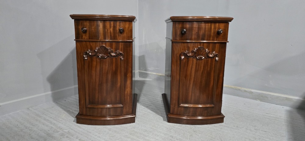 A matching pair of dark polished mahogany bedside cabinets featuring curved bow fronts, single drawers over cupboard doors, and carved decorative crestings. View II