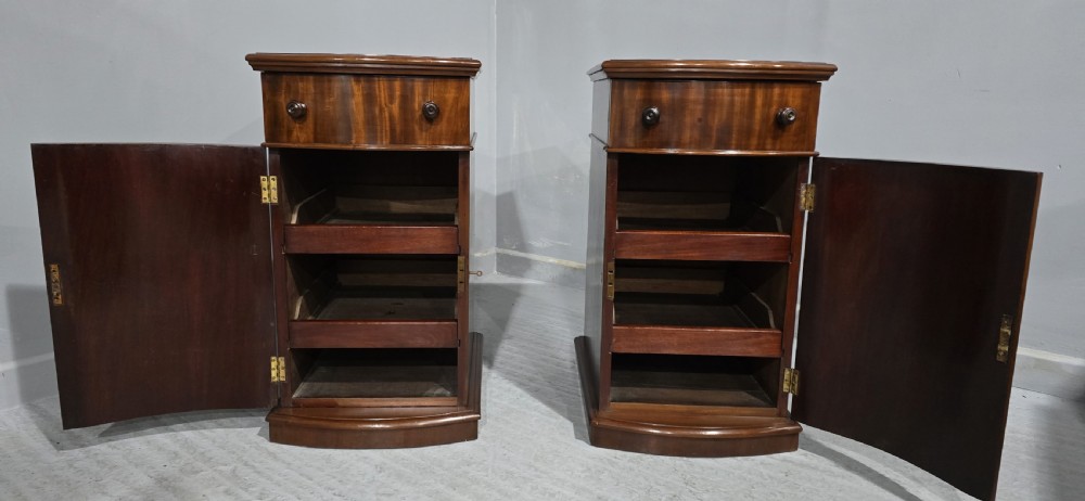 A matching pair of dark polished mahogany bedside cabinets featuring curved bow fronts, single drawers over cupboard doors, and carved decorative crestings. View III