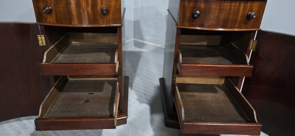 A matching pair of dark polished mahogany bedside cabinets featuring curved bow fronts, single drawers over cupboard doors, and carved decorative crestings. View V
