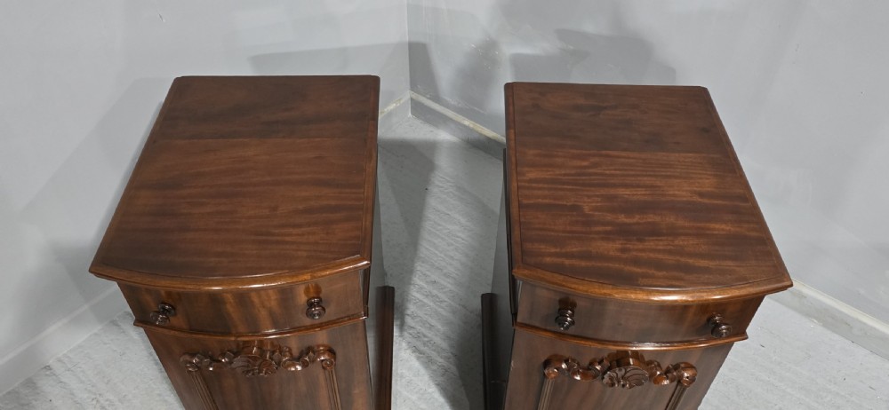 A matching pair of dark polished mahogany bedside cabinets featuring curved bow fronts, single drawers over cupboard doors, and carved decorative crestings. View VII