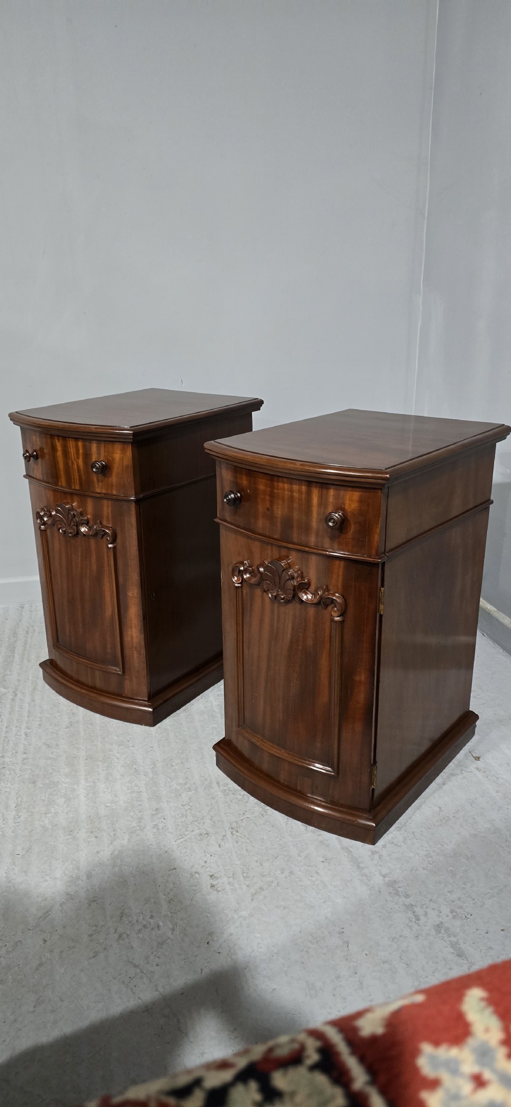A matching pair of dark polished mahogany bedside cabinets featuring curved bow fronts, single drawers over cupboard doors, and carved decorative crestings. View VIII