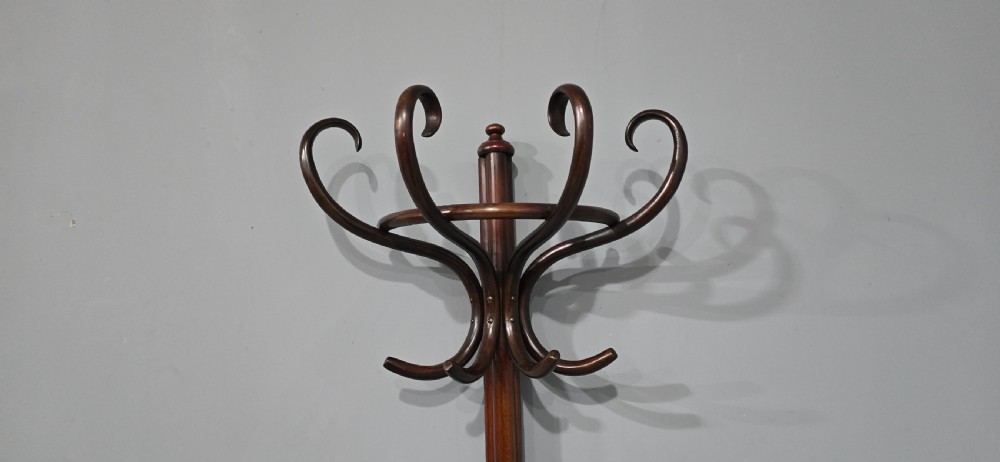 A tall dark brown bentwood coat stand featuring multiple scrolled upper hooks, a lower circular frame, and a four-footed arched base against a plain background. View III