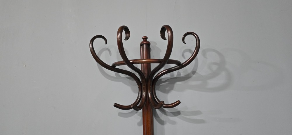 A tall dark brown bentwood coat stand featuring multiple scrolled upper hooks, a lower circular frame, and a four-footed arched base against a plain background. View IV