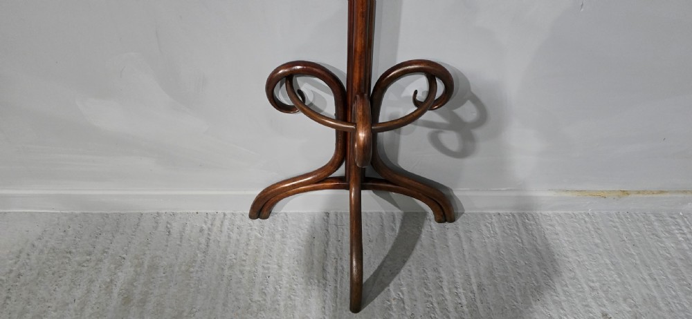 A tall dark brown bentwood coat stand featuring multiple scrolled upper hooks, a lower circular frame, and a four-footed arched base against a plain background. View V