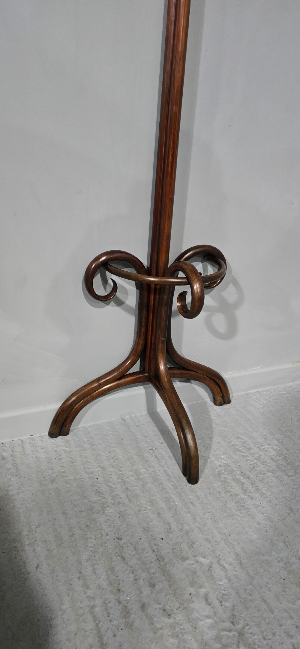 A tall dark brown bentwood coat stand featuring multiple scrolled upper hooks, a lower circular frame, and a four-footed arched base against a plain background. View VI