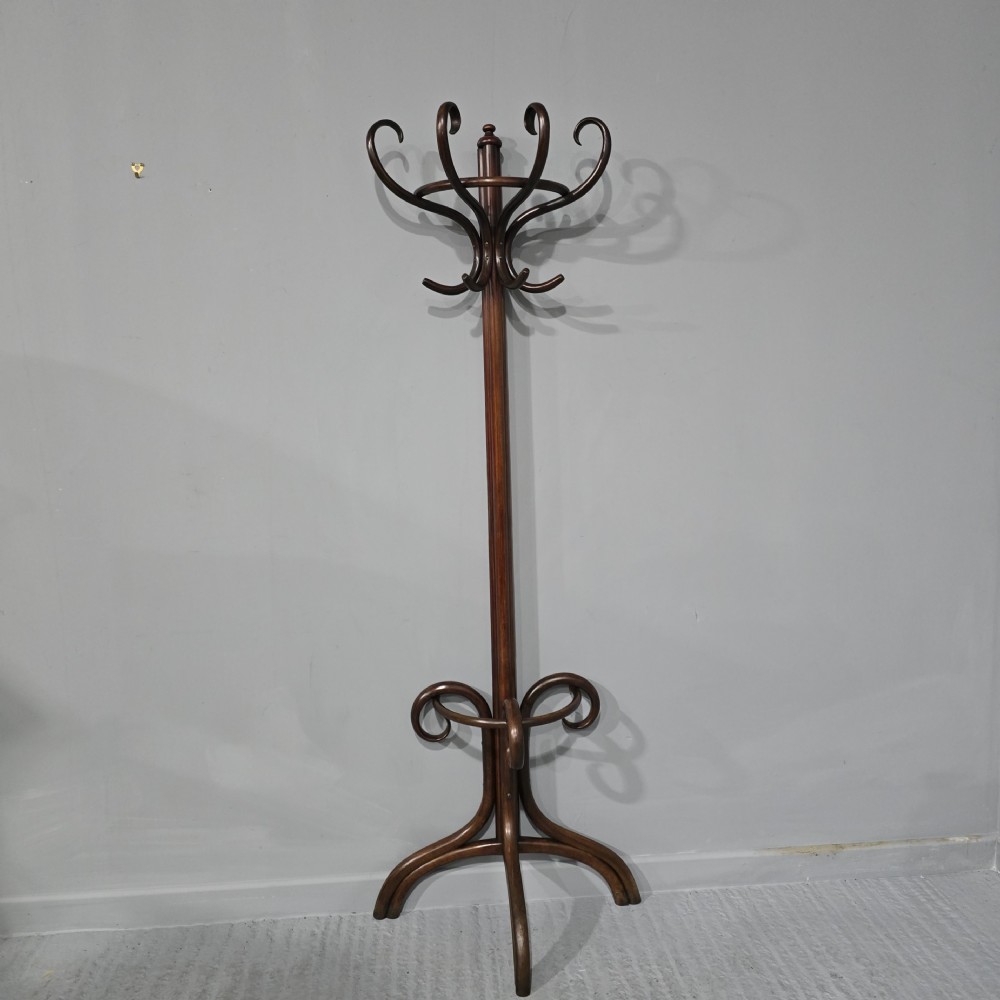 A tall dark brown bentwood coat stand featuring multiple scrolled upper hooks, a lower circular frame, and a four-footed arched base against a plain background.
