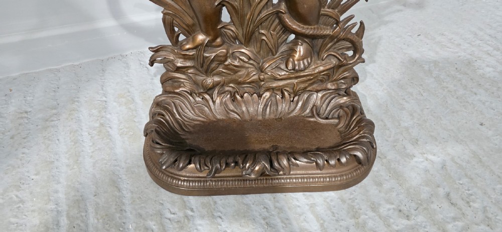 A dark bronzed cast iron stick stand featuring a sculpted figure of a child holding a coiled serpent on a leaf-patterned drip base. View V