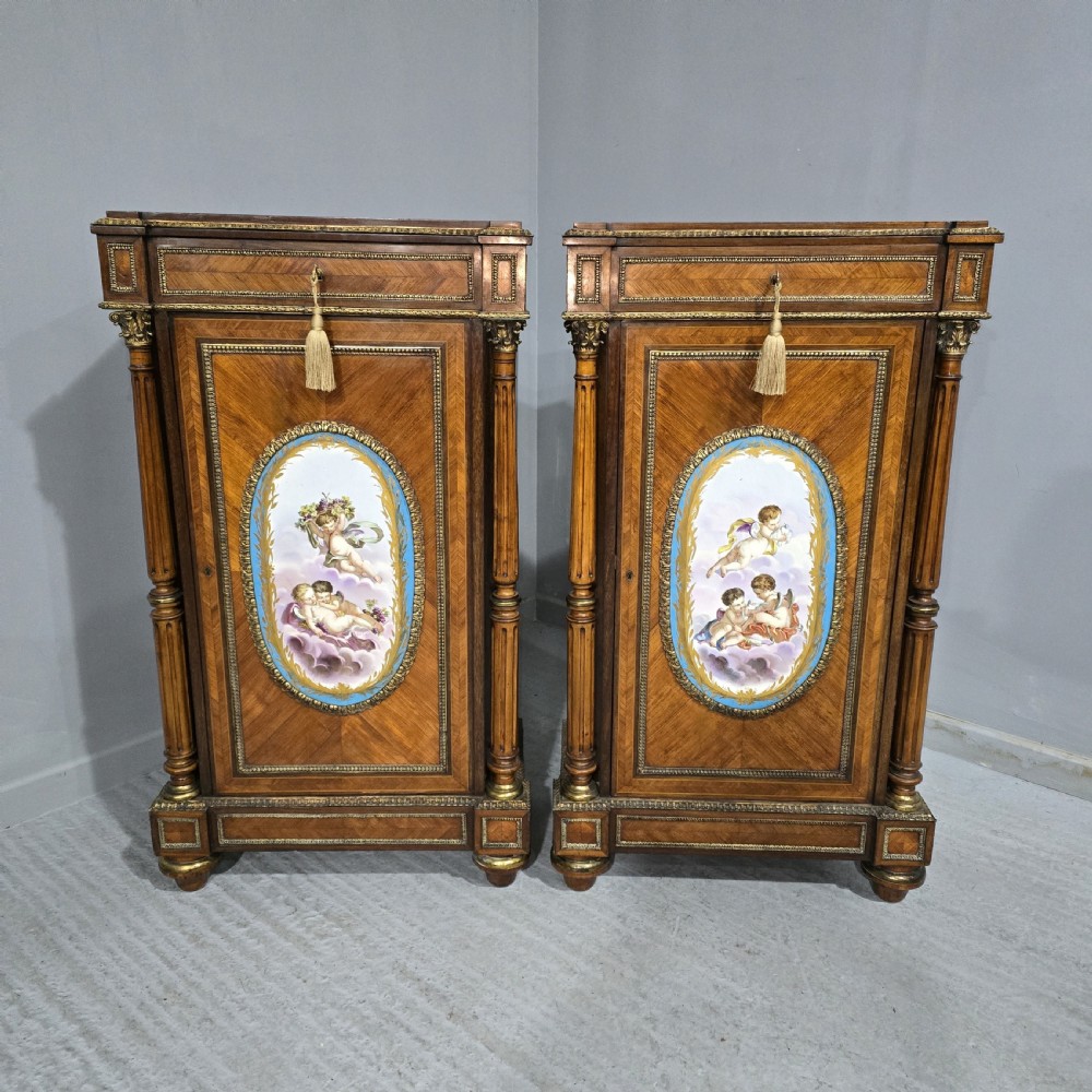 A pair of tall French Louis XVI style wooden side cabinets featuring parquetry veneers, fluted columns, gilt-bronze mounts, and central oval porcelain plaques painted with cherubs.