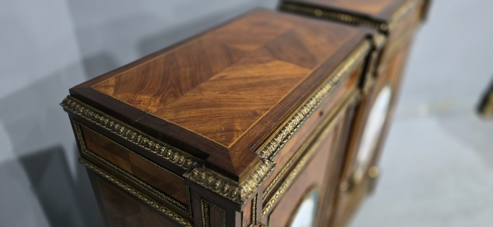 A pair of tall French Louis XVI style wooden side cabinets featuring parquetry veneers, fluted columns, gilt-bronze mounts, and central oval porcelain plaques painted with cherubs. View XVII