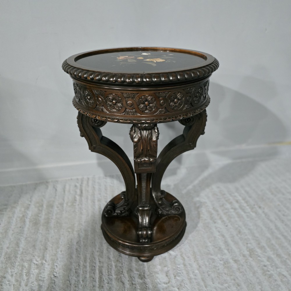 A Victorian dark carved timber side table with a circular black marble top featuring an inlaid floral pietra dura motif.