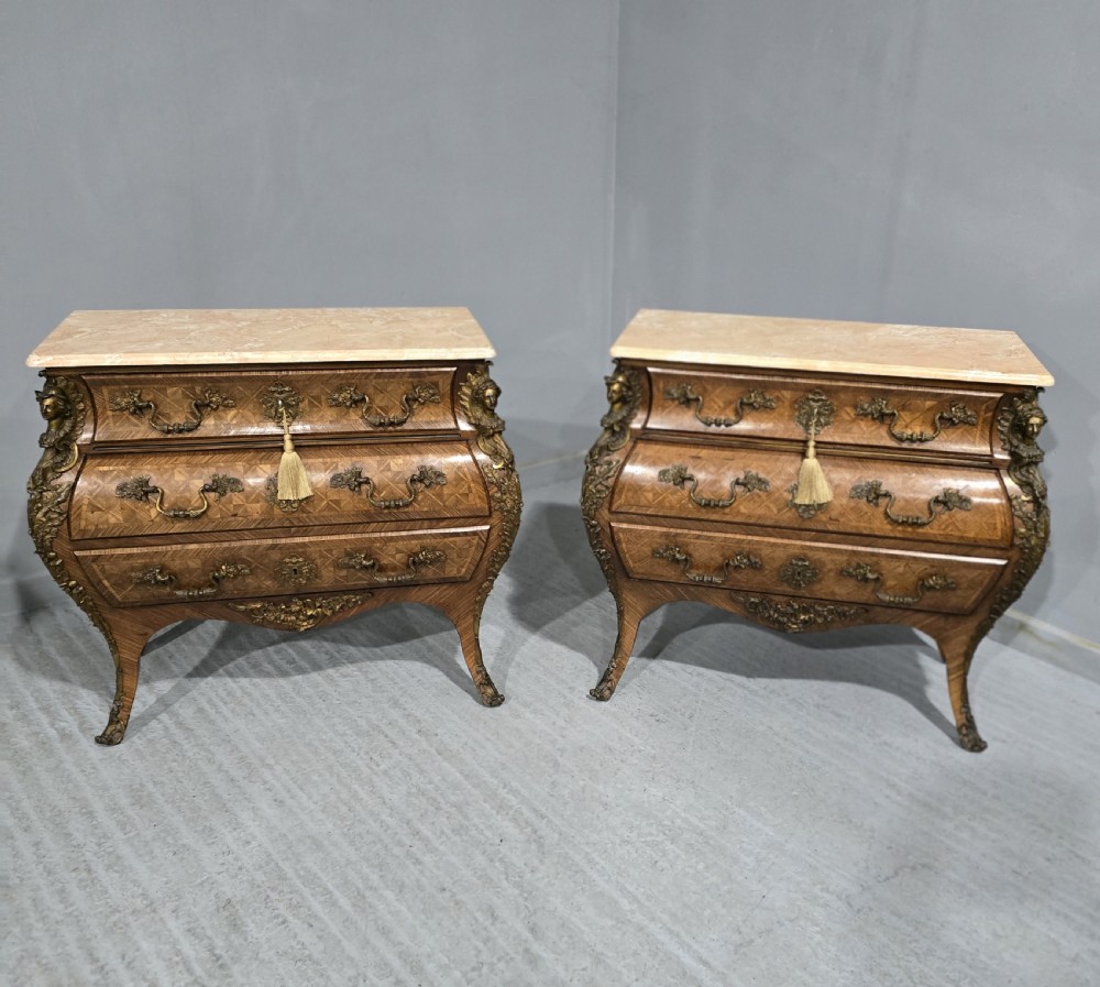 A pair of Louis XV style French bombe commodes featuring parquetry veneered drawer fronts, ornate metal mounts, and shaped marble tops.